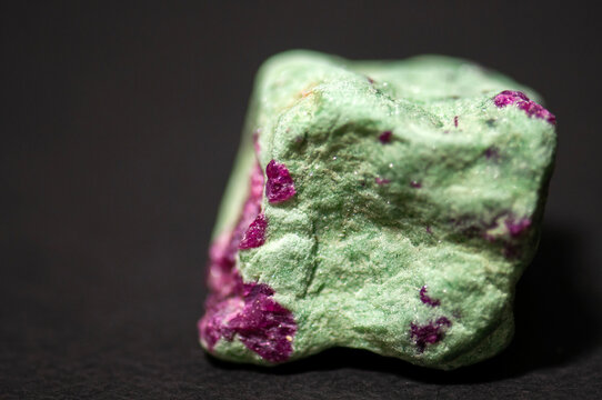 Raw ruby in zoisite mineral stone on a dark background. Natural green zoisite matrix with vibrant pink ruby crystals, macro close-up with detailed texture. Geological specimen and collectible mineral 