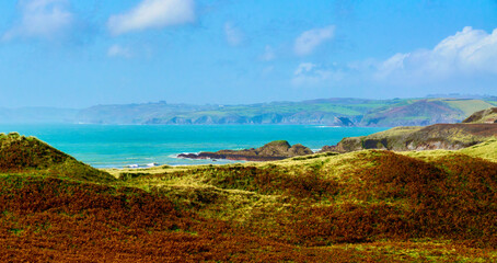 Rolling green and brown hills slope towards a vibrant turquoise ocean.