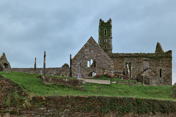 A medieval abbey and an ancient graveyard sit on a green hill under a cloudy Irish sky.