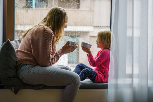 mother and daughter relaxing, drinks tea by window on rainy day, Cozy, Home, Lifestyle, Indoor, Relaxation, Comfort
