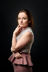 Obraz premium A woman in a pink skirt and a white lace top stands in a dark studio.