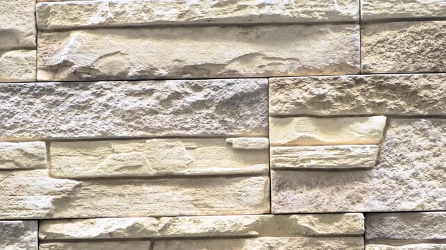 Textured stone wall with light-colored, unevenly shaped stones arranged in a horizontal pattern. Ideal for backgrounds or architectural designs.