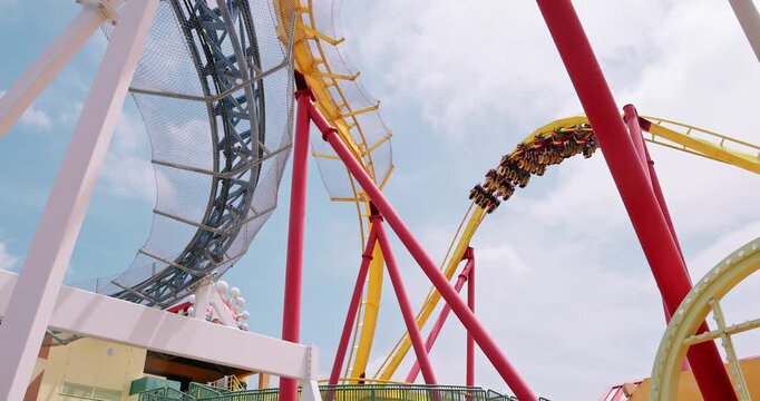 Roller coaster train carrying passengers descending on yellow track at amusement park under blue sky. theme park, adrenaline, summer vacation, family fun, entertainment, thrill ride.