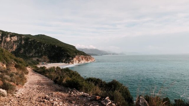 Stable tripod shot of dramatic coastal cliffs and turquoise sea. Layered mountain background, soft daylight and clean horizon create a balanced cinematic landscape composition.