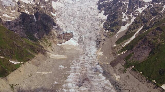 Aerial drone view of a steep glacial cirque in Svaneti, Georgia, with debris covered ice, flow bands, moraines, meltwater pools, thin waterfalls, and a striated terminus.