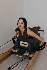 Pilates Reformer machine with Pilates box attachment in use by a slim athletic model. She performs controlled exercises on the apparatus, demonstrating effective training.