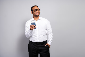 Young handsome businessman at the office smiling while using a smartphone in a white shirt and...