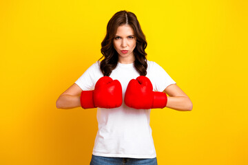 Young chic woman in white tshirt wearing red boxing gloves poses with determined expression against...