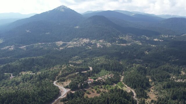 Forested conical mountain above village valley with winding mountain roads