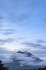 Majestic Volcanic Peak Shrouded in Low Clouds under a Blue Twilight Sky in Tropical Highlands