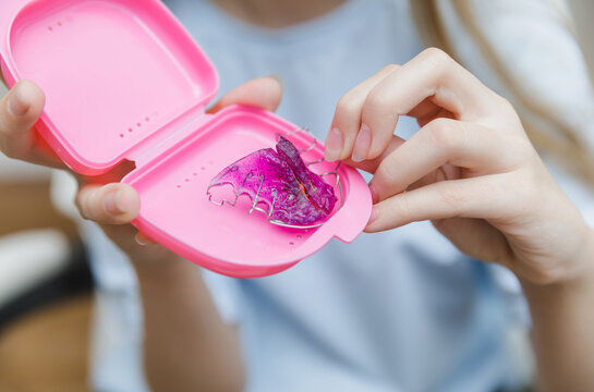Teenage girl hands holding pink plastic case with purple orthodontic plate, pediatric dentistry and removable appliance storage and care concept