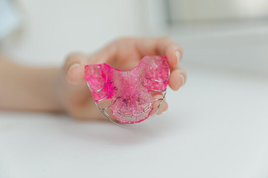 Close up of pink removable orthodontic dental plate held by fingers, pediatric dentistry and tooth alignment correction device concept