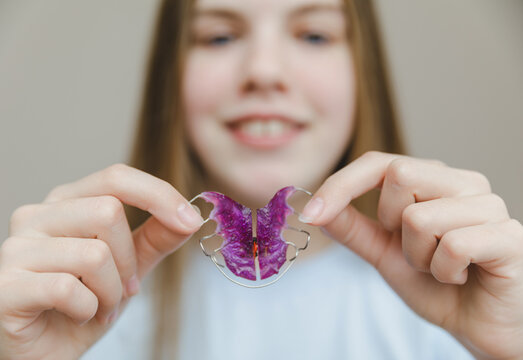 Smiling teenage girl holding pink removable orthodontic plate in front of her face, pediatric dentistry and professional bite correction concept