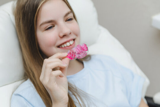 Smiling teenage girl in a dental chair looking at her purple orthodontic plate, pediatric dentistry and positive experience with bite correction concept