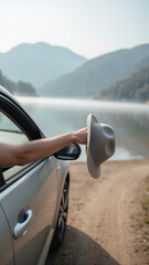 Car hand hat lake mountain road travel outdoor summer adventure Relaxing drive by lake with hand holding hat surrounded by mountains and nature
