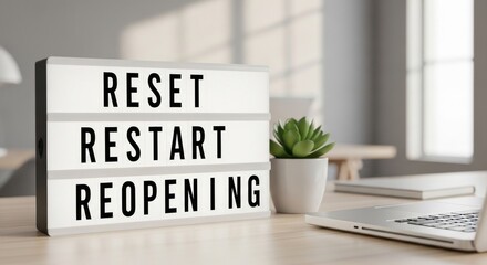 Fototapeta premium A lightbox with the words 'Reset, Restart, Reopen' on a wooden desk with a laptop and a plant.