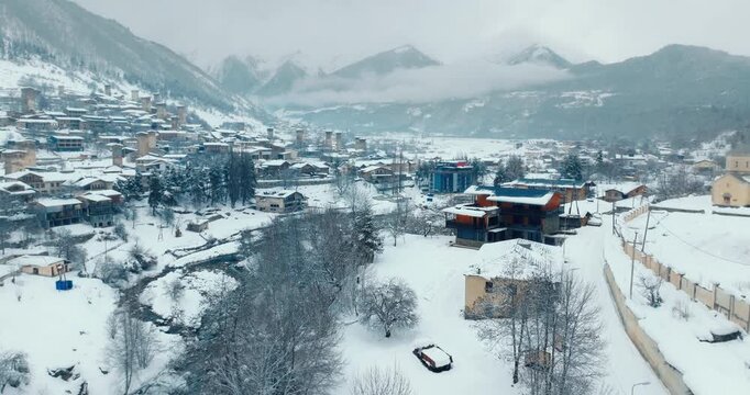 Aerial drone shot flying over a snow-covered town towards historic Svan towers in Mestia, Georgia. Winter landscape and Caucasus mountains with forward camera movement.