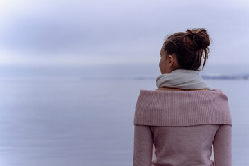 Fototapeta premium young woman in pink top and white scarf looking out to a lake with dark clouds with negative space for text