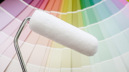 Obraz premium Paint roller ready for use, placed against a fanned-out color palette, representing renovation and interior design choices