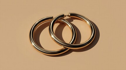 Two substantial, polished, golden hoop earrings resting upon a smooth, muted beige surface.