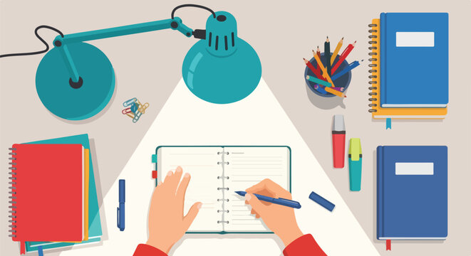 Top view of a desk with a person writing in a planner, surrounded by books, pens, and a desk lamp illuminating the workspace.