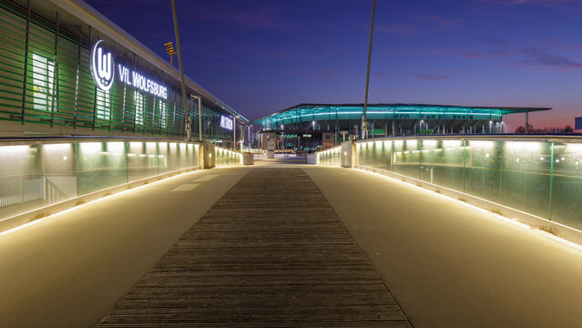 Wolfsburg, Deutschland &ndash; 17. November 2018: Blick &uuml;ber eine beleuchtete Fu&szlig;g&auml;ngerbr&uuml;cke auf das AOK Stadion des VfL Wolfsburg sowie die benachbarte Volkswagen Arena am Abend. Moderne Sportarchitektur 