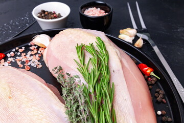 Raw chicken breasts with herbs, spices, and garlic on a black surface ready for meal preparation in a kitchen setting