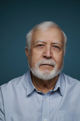 Obraz premium Senior man with white beard and blue shirt poses in front of blue background during indoor session