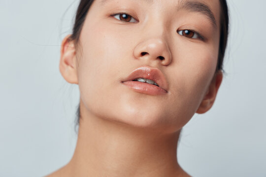 Portrait of a young woman with clear skin and natural makeup looking at camera with neutral expression. Closeup face with smooth complexion and glossy lips on neutral background.