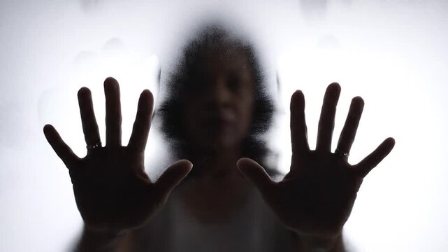 Silhouette of hands pressed against a frosted glass surface illustrating a concept of barrier and emotional struggle
