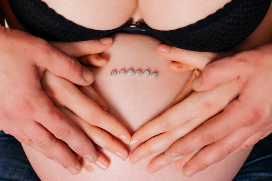Pregnant woman belly with hands and dermal piercings