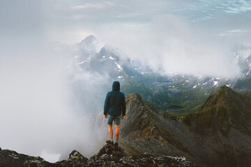 Man tourist travel in Norway solo standing on cliff climbing foggy mountains in Lofoten islands,...
