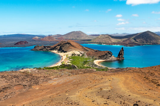 Picturesque view of Bartolome Island in the Galapagos Archipelago. The landscape features a mix of rugged volcanic terrain and lush green areas, with a prominent rock formation.