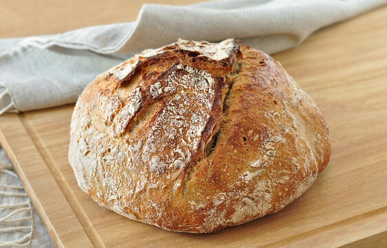 Round sourdough bread loaf, with a crispy crust, dusted with flour, resting on a rustic linen cloth on a wooden surface. Home bakery, traditional baking concept. Realistic image, Negative space