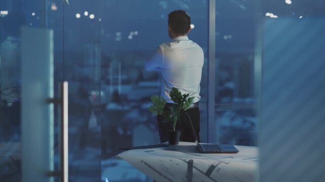Business manager ponders crucial selections while observing brightly lit urban skyline from office window