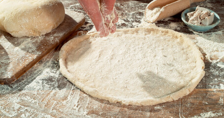Falling flour dusting freshly kneaded pizza dough on wooden table. Cinematic baking concept, preparation of homemade pizza and yeast dough.