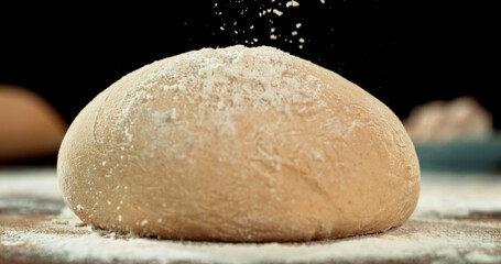 Obraz premium Static shot of a leavened dough loaf isolated on black background with falling flour. Concept of baking, artisan bread making and dough preparation.