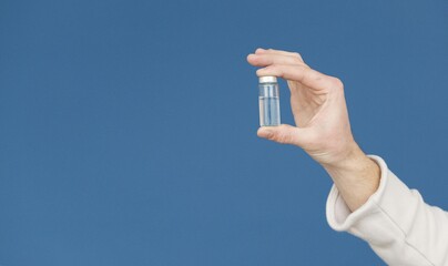 Hand Holding a Medical Vial with Clear Liquid Against a Blue Background
