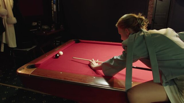 Evening game of pool craftsmanship and setting for refining pool shooting techniques. Serene environment where adult woman in hones delicate bank shot skills on red felt pool table in billiards club