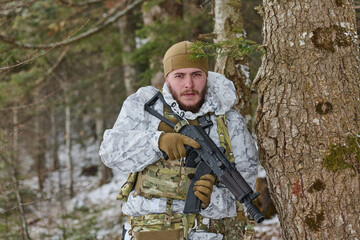 Obraz premium Soldier In Winter Camouflage Holding Rifle While Hiding Behind Tree In Snowy Forest