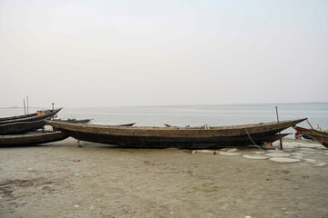 Obraz premium Numerous wooden boats rest on a sandy shore beside a vast body of water under a hazy sky