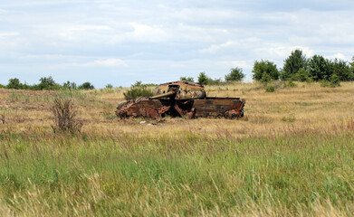 Fototapeta premium A destroyed, rusting tank in a meadow. A battlefield, war, a combat training ground.
