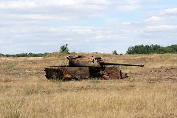 Fototapeta premium A destroyed, rusting tank in a meadow. A battlefield, war, a combat training ground.