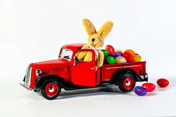 red classic toy pickup truck with Easter bunny and colorful jelly beans on white background
