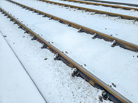 Parallel railway tracks cut through a blanket of fresh snow, their steel rails contrasting against the white surface, capturing a quiet winter moment with crisp textures and a sense of industrial stil