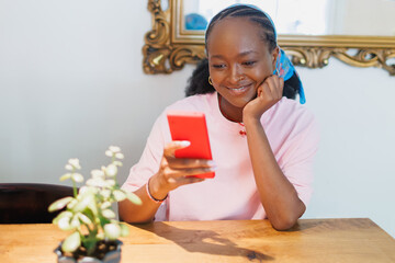 Young woman enjoys using smartphone at a table in a cafe during the day while looking at the screen with a smile