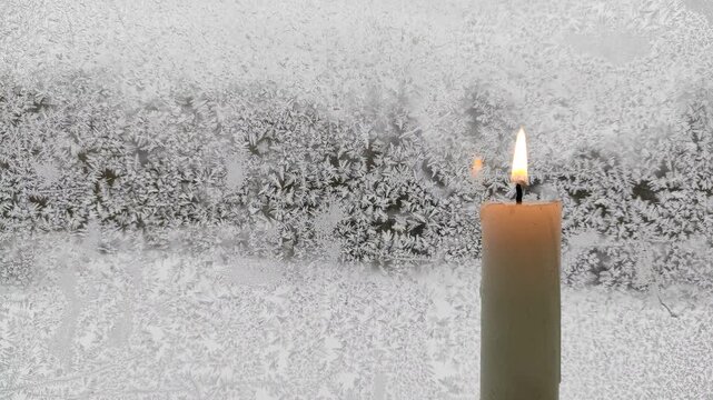 A candle burns against the background of a frozen window №4