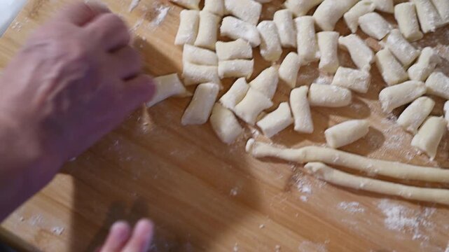 Woman making homemade pasta potato gnocchi. Dropping the dough pieces onto the floured wooden table.
