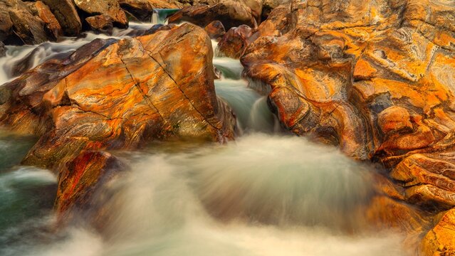 Flowing River Water Over Textured Orange Rock Formation, Verzasca Valley, Switzerland