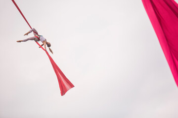 Aerial silk session in a park, featuring a performer upside down on red silks during daytime © prelevicm